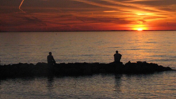 Un coucher de soleil sur une étendue d’eau, avec deux silhouettes se détachant sur un promontoire rocheux.