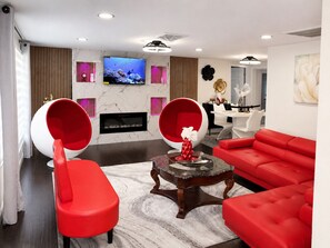 Una sala moderna con chimenea, asientos rojos, televisor y comedor.