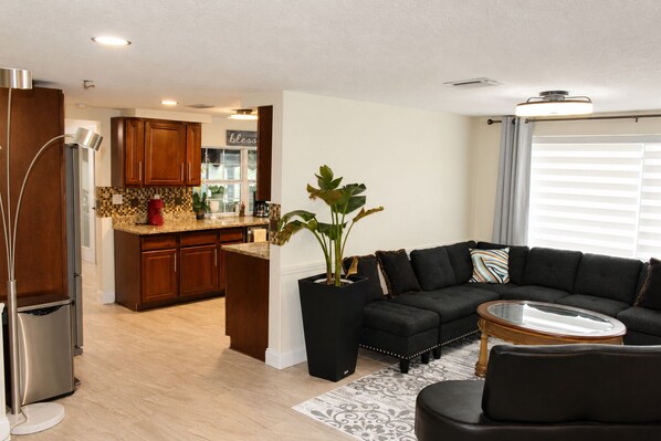 A modern living room with a dark sofa, a glass coffee table, and a potted plant.