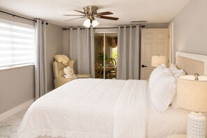 Ein Schlafzimmer mit einem Bett, einem Deckenventilator, einem Sessel mit Kissen, einer Lampe und einer Tür.