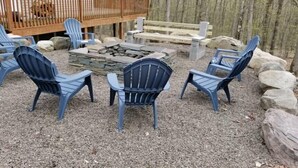 An outdoor seating area with Adirondack chairs and a stone fire pit, surrounded by rocks and a wooden deck. - MASTHOPE-BIG BEAR-LACKAWAXEN-LUXURY 4 Bedroom-Game Room (Lackawaxen)