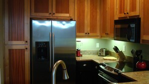 A kitchen with wooden cabinets, a stainless steel refrigerator, a microwave, a toaster, and a sink with a faucet.