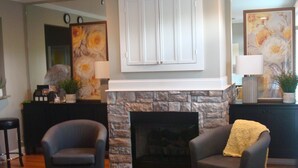 A living room with a stone fireplace, two armchairs, a coffee table, and a sideboard with decorative items.