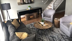 A modern living room with a grey sofa set, a round coffee table with a plant, a black side table, and a staircase in the background.