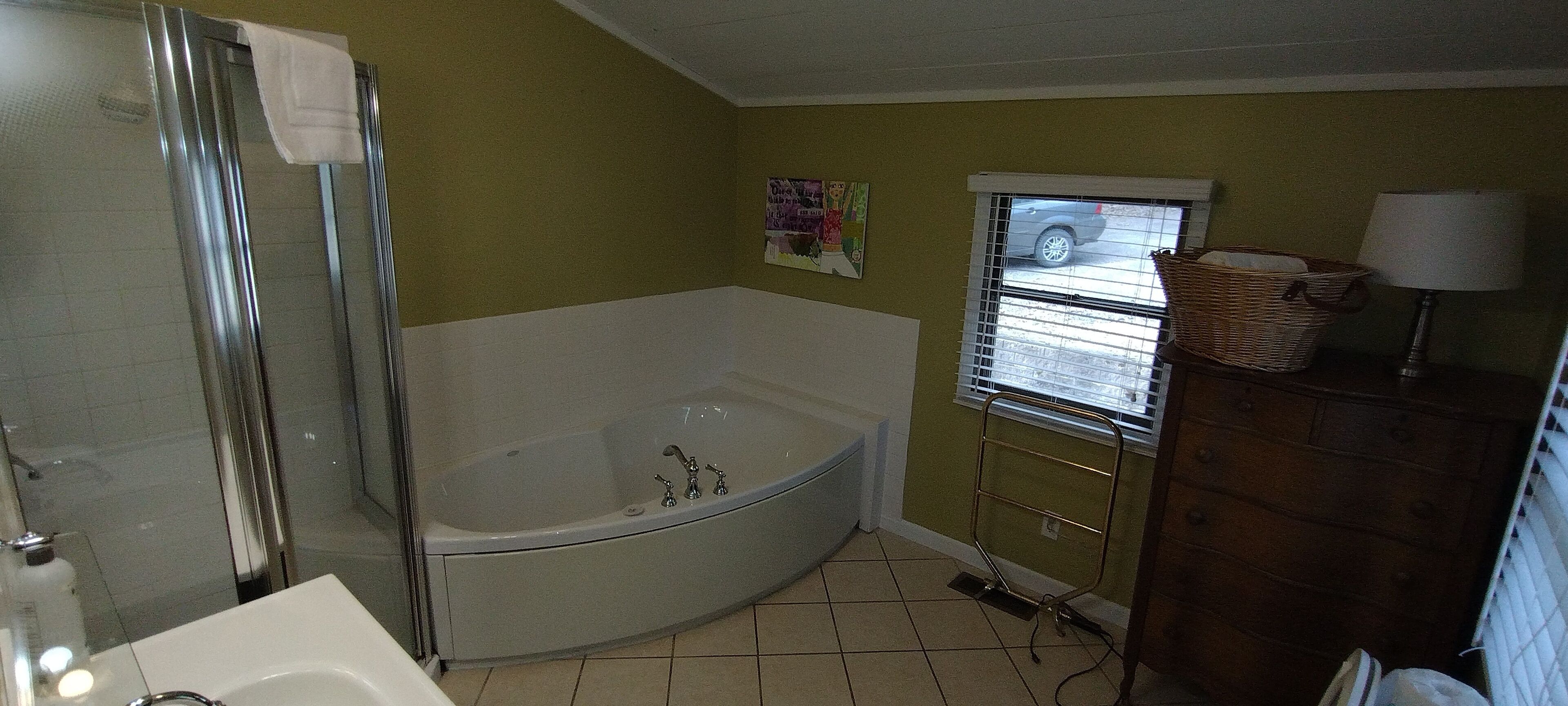 Een badkamer met een inloopdouche, een bad, een wastafel en een raam met zonwering.