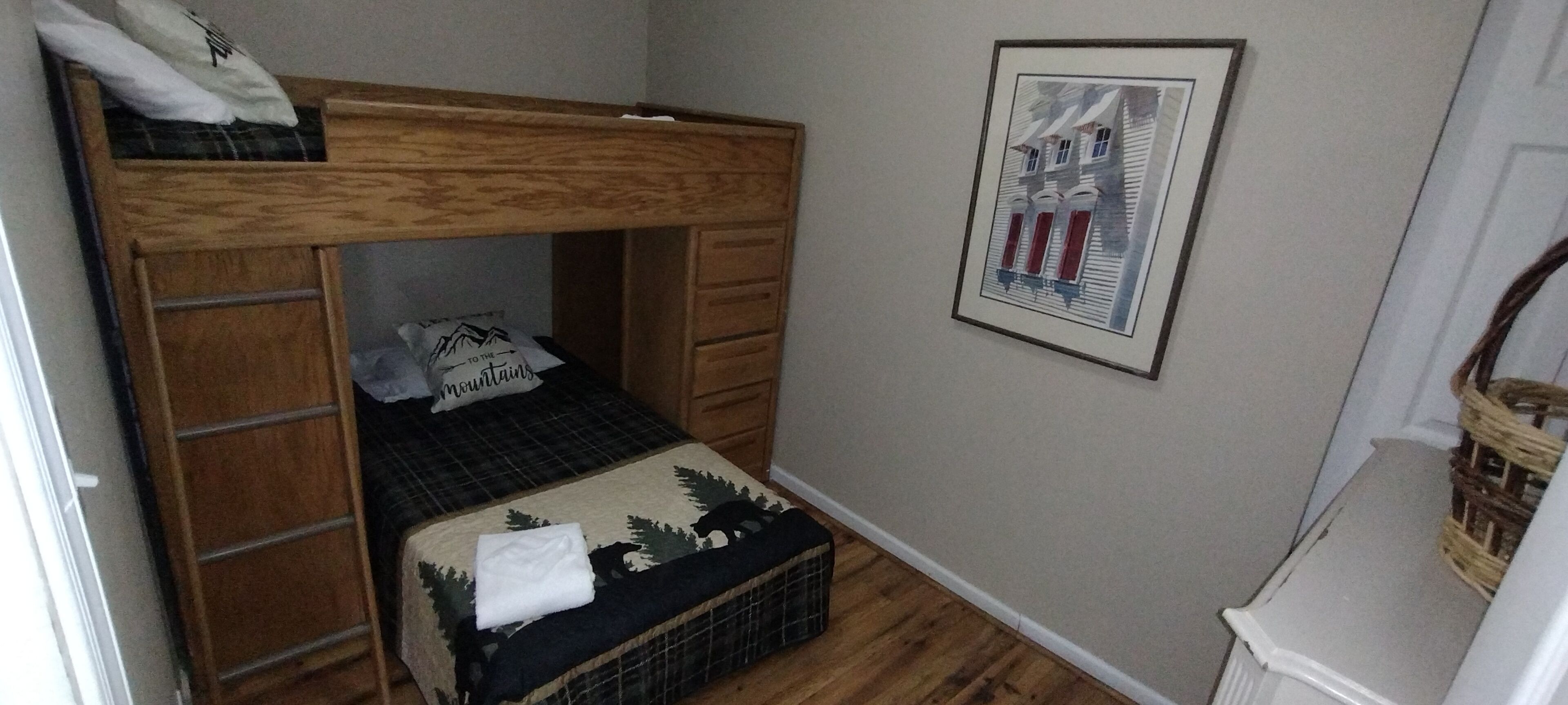 Una cama litera con estructura de madera, una mesita de noche pequeña y un cuadro enmarcado en la pared.