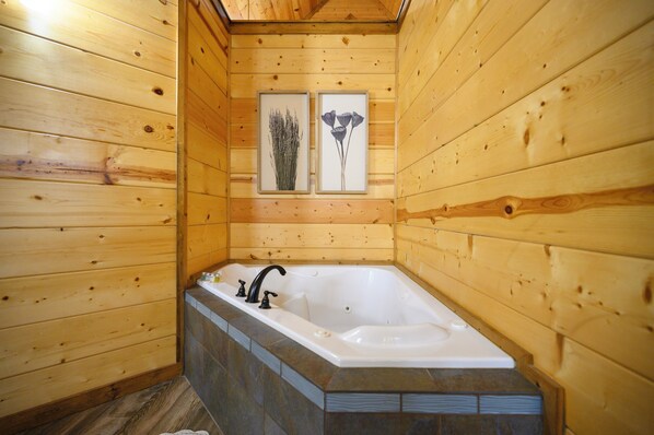 A wooden cabin interior with a bathtub, wooden walls, and two framed pictures.