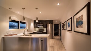 Une cuisine moderne dotée d’un îlot central, d’appareils électroménagers en acier inoxydable, de luminaires suspendus et d’œuvres d’art encadrées accrochées aux murs.
