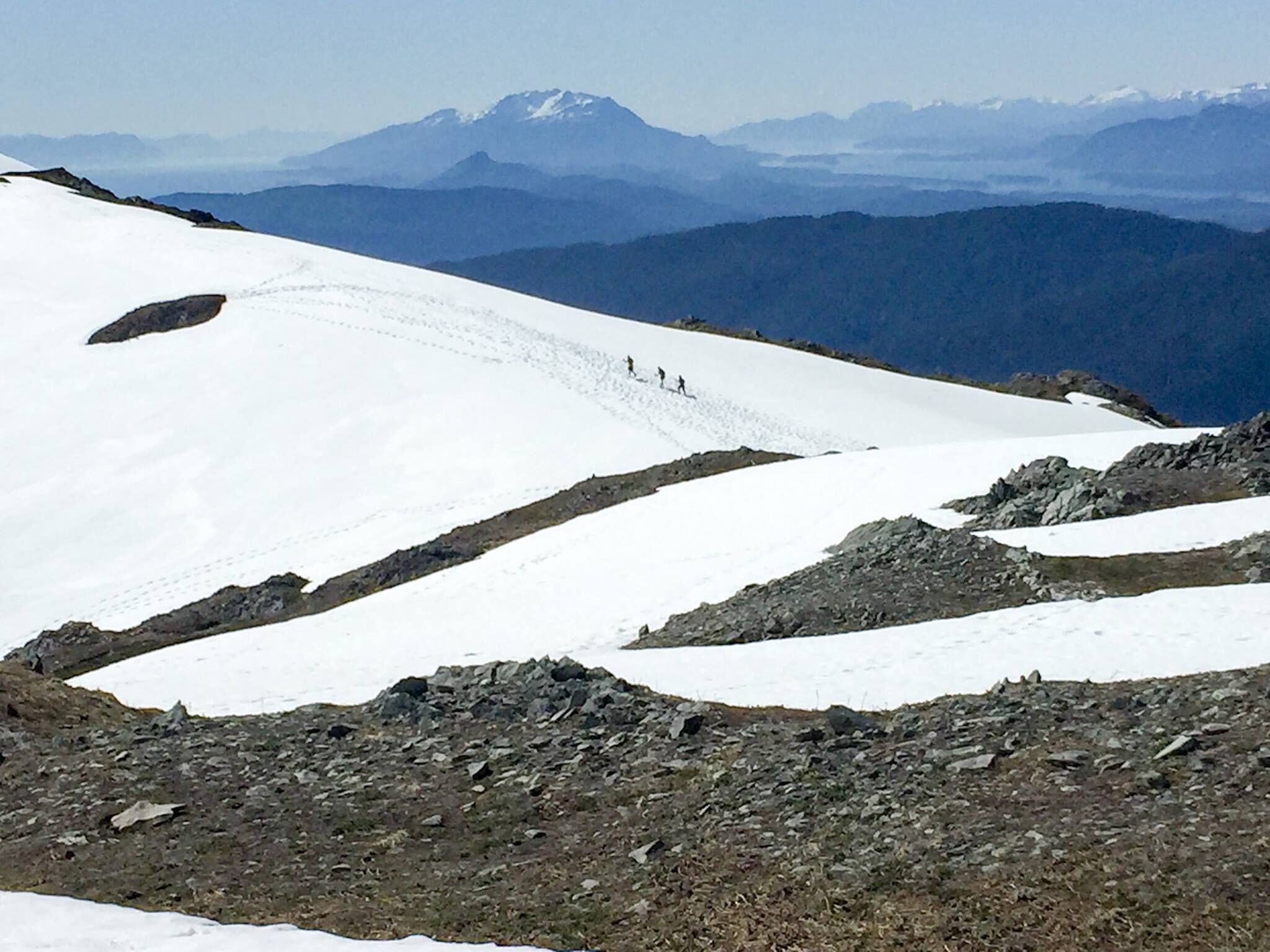 A snow-covered mountain slope with a clear path and distant mountains.