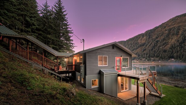 Un chalet au bord du lac, doté d’une terrasse, d’un escalier et offrant une vue sur le lac et les montagnes.