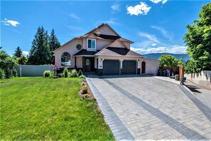 A two-story house with a driveway leading to a garage, surrounded by a well-maintained lawn and trees.