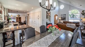 A modern kitchen with a central island, dining area with chairs, and a living room with a sofa and a coffee table.