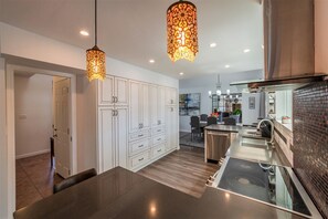 Cozinha moderna com bancada escura, armários brancos e luminária pendente.