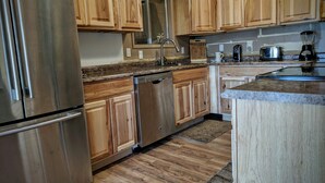 Cocina con gabinetes de madera, electrodomésticos de acero inoxidable y encimera de granito.