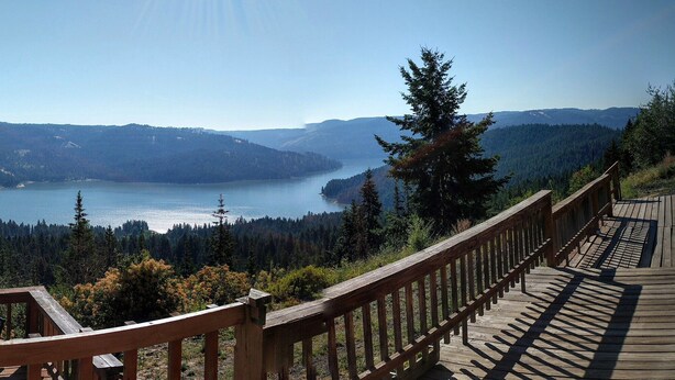 Una terraza de madera con vista a un lago rodeado de colinas boscosas.