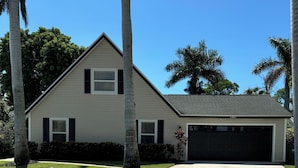 A two-story house with a garage, surrounded by palm trees and a well-maintained lawn.