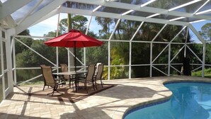 A covered outdoor area with a pool, patio furniture, and a red umbrella.