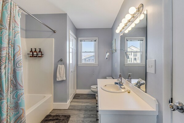 A bathroom with a bathtub, a vanity with a mirror and lights, and a shower curtain. - Spring Break Sale! Just 2 min walk to Beach + Canalfront, Beach Esssentials (Holden Beach)