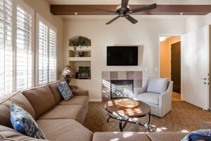 A living room with a sofa, a coffee table, a fireplace, a television, and a ceiling fan.