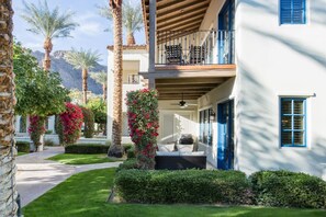 A two-story building with a balcony, a covered patio, and a well-maintained garden with palm trees and flowering plants.