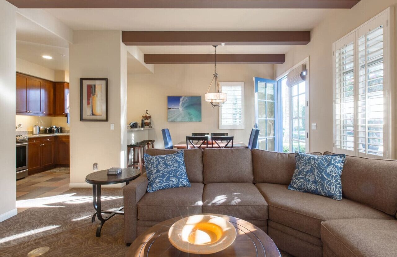 A modern living room with a sectional sofa, a coffee table, and a dining area with a chandelier.