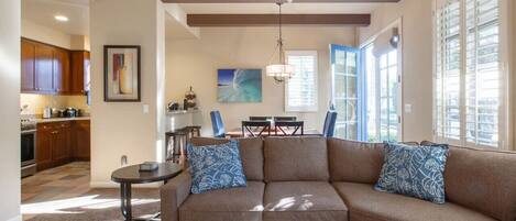 A modern living room with a sectional sofa, a coffee table, and a dining area with a chandelier.