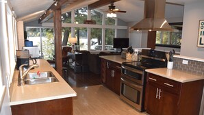A modern kitchen with wooden cabinets, a stainless steel sink, and a large window overlooking a deck.