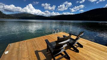 A wooden dock with a bench and a ladder, overlooking a calm lake with mountains in the background.
