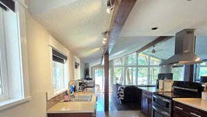 A spacious kitchen with a central island, dark wooden bench, and large windows offering natural light.