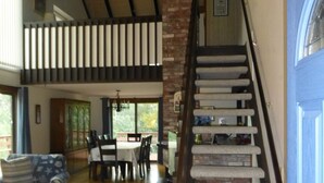 A spacious living area with a high ceiling, a staircase with a handrail, and a dining area with chairs and a table.