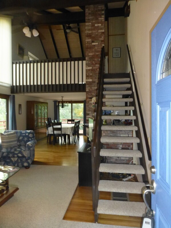 A spacious living area with a high ceiling, a staircase with a handrail, and a dining area with chairs and a table.