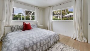Ein Schlafzimmer mit Bett, zwei Fenstern, Deckenventilator und Blick auf Grünfläche.