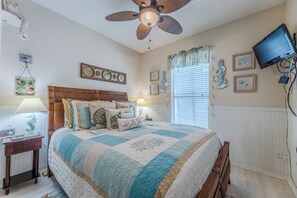 A bedroom with a bed, a ceiling fan, a TV, and wall decorations. - Private Pool, Small pets welcome, walk to beach, bikes and golf cart included (Destin)