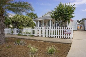 A single-story house with a white picket fence, a porch with columns, and a sign for Castaway Cottage. - Private Pool, Small pets welcome, walk to beach, bikes and golf cart included (Destin)