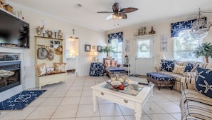 A cozy living room with a fireplace, striped sofa, and nautical-themed decor. - Private Pool, Small pets welcome, walk to beach, bikes and golf cart included (Destin)
