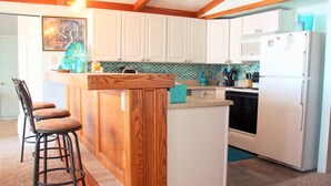 A kitchen with white cabinets, a wooden island with bar stools, a refrigerator, and a tiled backsplash. - Lake front (Sunrise Beach)