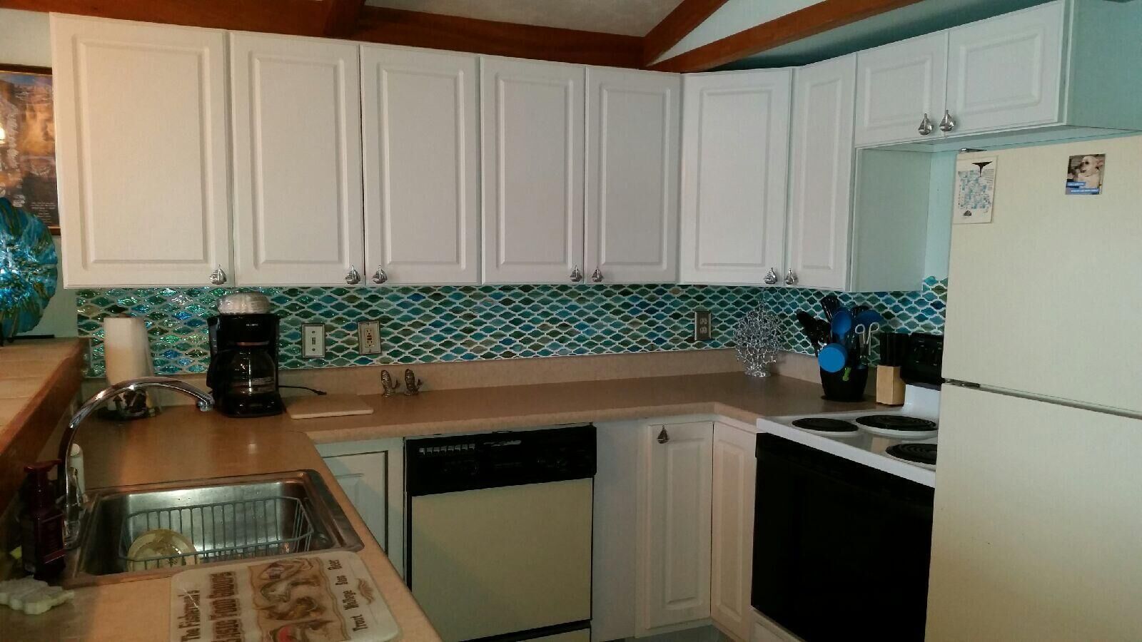 Una cocina con armarios blancos, lavavajillas, estufa y refrigerador.