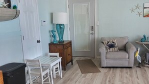 A living room with a wooden floor, a striped armchair, a small table with chairs, a lamp, and a door. - Lake front (Sunrise Beach)