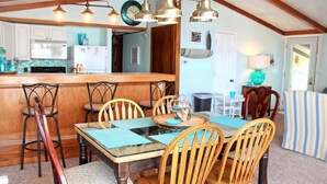 A dining area with a wooden table and chairs, a kitchen in the background, and pendant lighting. - Lake front (Sunrise Beach)