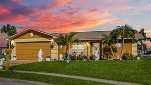 A two-story house with a garage, a front lawn, and palm trees. - Luxurious Waterfront Holiday Home with Fully Encompassing Lakeview  (Holiday)