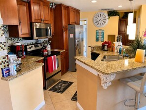 A kitchen with wooden cabinets, stainless steel appliances, a granite countertop, and a clock on the wall. - Luxurious Waterfront Holiday Home with Fully Encompassing Lakeview  (Holiday)