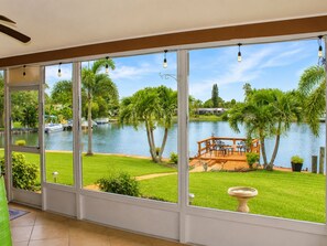 A large glass door leading to a deck with a view of a lake, palm trees, and a boat.
