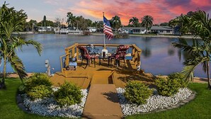 A waterfront deck with outdoor seating, a flag, and a view of the lake and surrounding houses. - Luxurious Waterfront Holiday Home with Fully Encompassing Lakeview  (Holiday)