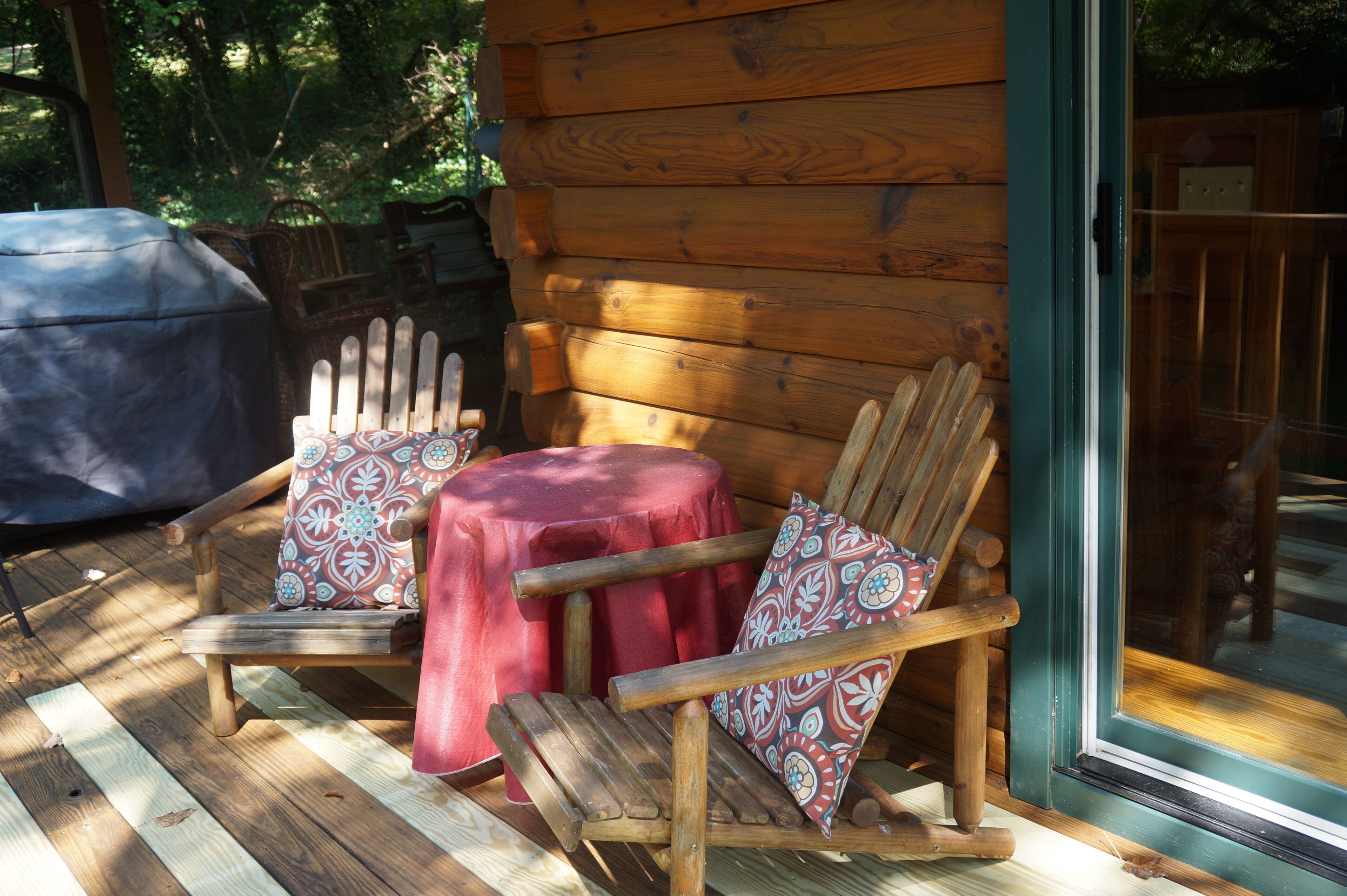Una terraza de madera con una mecedora y una mesita pequeña, ambas con cojines estampados.