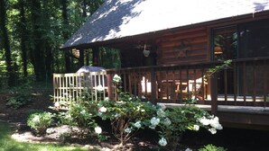 Een houten hut met een veranda, omringd door een tuin met witte bloemen en een waterslang.