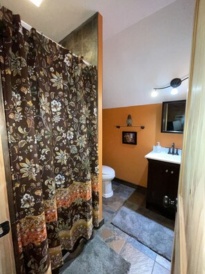 Un baño con cortina de ducha, inodoro, lavabo y piso de baldosas.