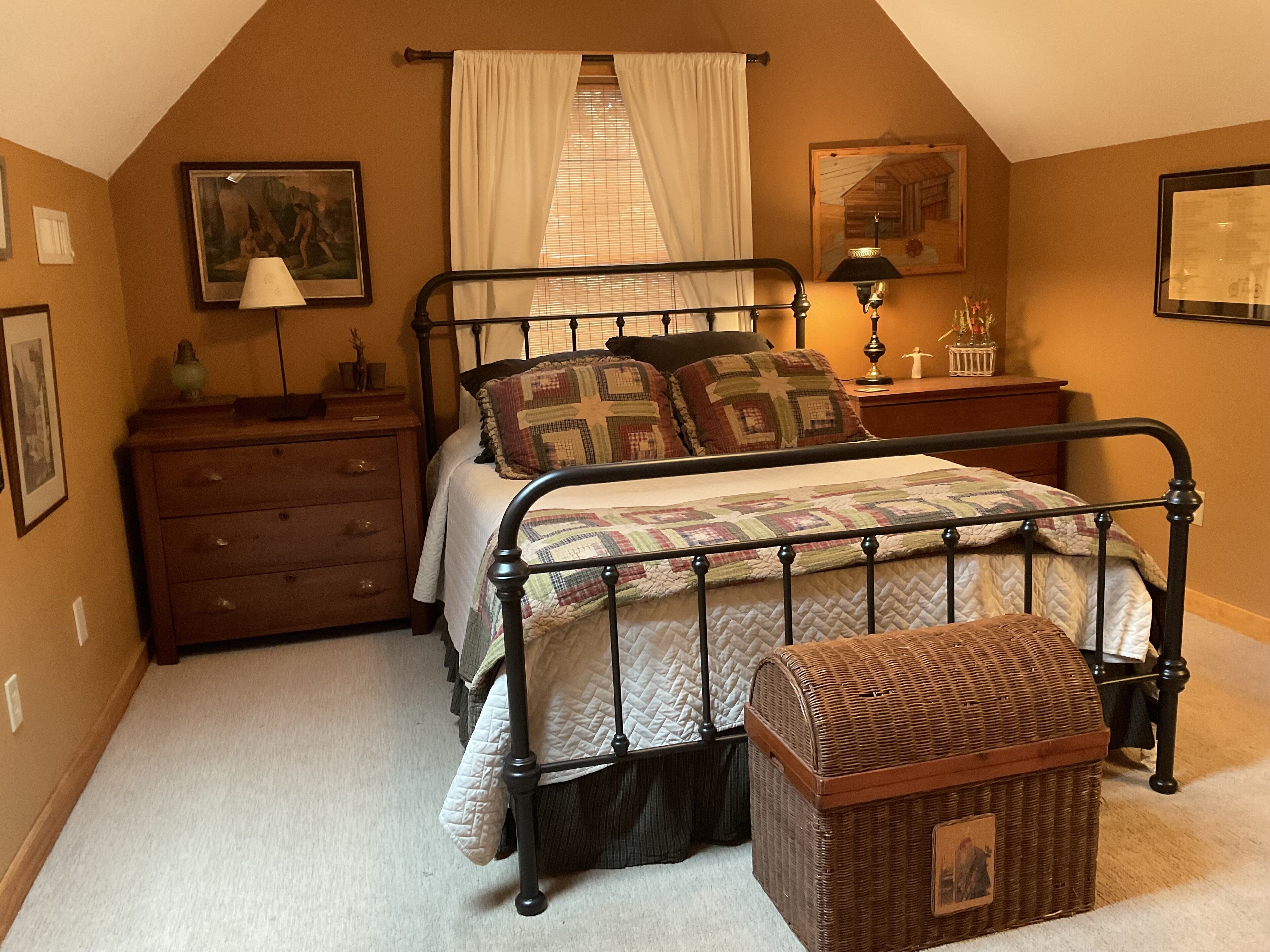 Ein Schlafzimmer mit Bett, Schminktisch, Nachttisch, Lampe und einem Korbwäscheschrank.