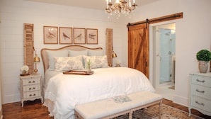 A bedroom with a large bed, a bench, a dresser, a nightstand, a chandelier, and a sliding door closet. - Historic Southern Cottage close to Downtown Conway (Conway)