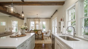 A spacious kitchen with a large island, wooden beams, and a view of greenery outside. - Historic Southern Cottage close to Downtown Conway (Conway)