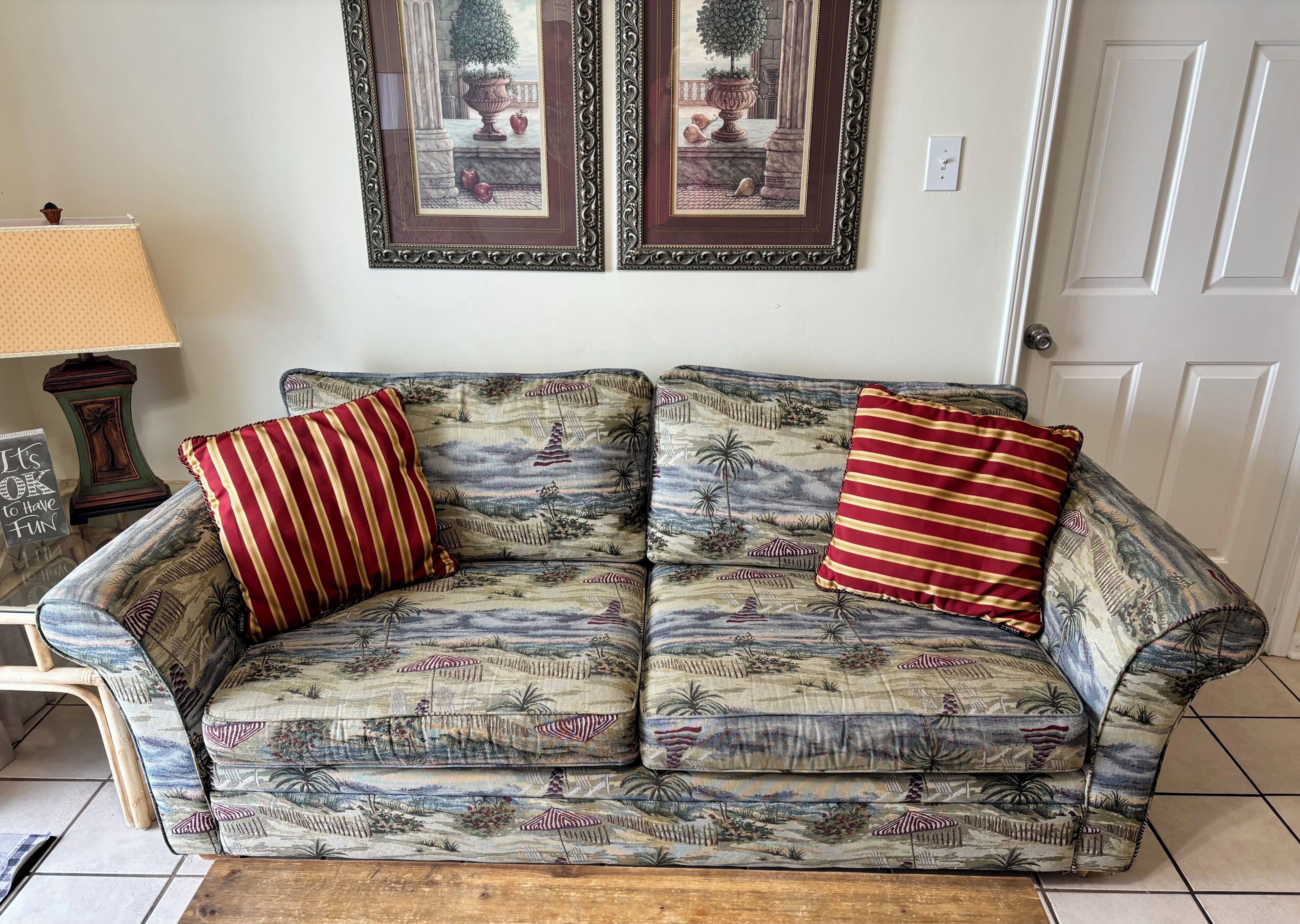 A patterned sofa with striped pillows, a lamp, and two framed artworks on the wall.